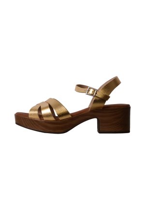 Sandale en cuir doré avec talon bloc en bois, trois brides croisées sur les orteils, bride de cheville avec fermeture à boucle.