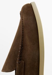 Bruine suède instapschoen met gedetailleerd stiksel en een beige rubberen zool, weergegeven vanuit een close-up zijaanzicht.