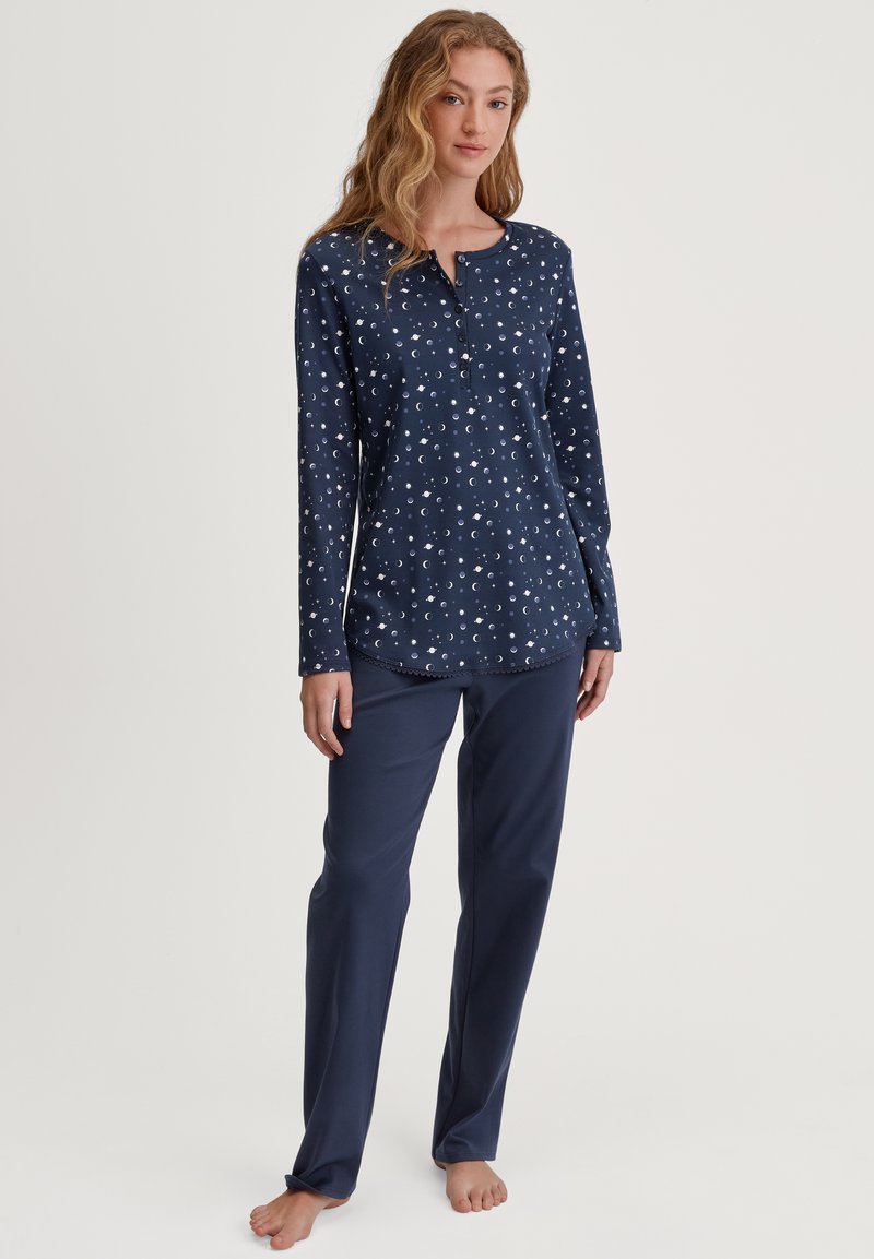 Set di pigiami blu navy composto da una maglietta a maniche lunghe con stampa di lune crescenti bianche, scollatura a bottoni e pantaloni coordinati in tinta unita. Tessuto morbido.