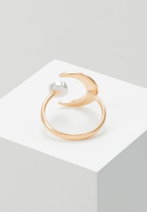 Goldener offener Ring mit einem Halbmond an einem Ende und einem kleinen silbernen Zylinder am anderen, dargestellt auf einer weißen Oberfläche.