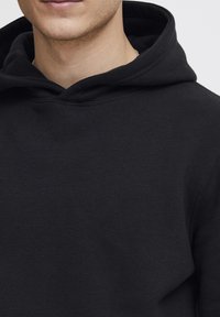 Sudadera con capucha negra que presenta una textura suave, un diseño casual y un escote amplio. La tela parece resistente pero cómoda.
