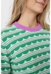 Pull vert et blanc à motifs avec un col côtelé lilas, présentant des motifs ondulés en forme d'écailles et des rayures horizontales. Texture en maille douce.