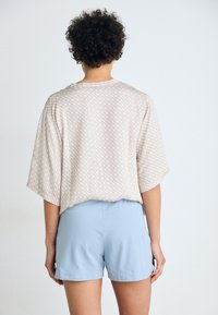 Lichtbeige T-shirt met korte mouwen en een textuurpatroon, gecombineerd met lichtblauwe shorts. Gladde stof, ontspannen pasvorm en eenvoudig ontwerp.