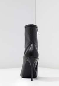 Stivali alla caviglia in pelle nera con tacco a spillo alto, texture liscia, zip laterale e dettagli di cucitura a contrasto.