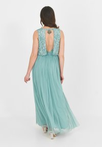Mint green maxi dress with a sequined back, deep neckline, and flowing skirt. Textured bodice and smooth, lightweight fabric.
