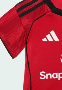 Crvena sportska majica s crnim detaljima, kratkim rukavima i strukturiranom tkaninom. Na prsima i ramenu prikazuje bijeli logo.