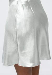 Zilverkleurige metallic A-lijn rok gemaakt van een glad, glanzend materiaal met een zachte val, voorzien van een afgeronde zoom en nette stikseldetails.