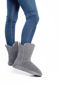 Botas de tobillo de ante gris con forro de piel, puntera redondeada y detalles de costura, combinadas con jeans skinny de mezclilla azul.