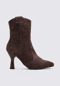 Bottines en daim brun avec un bout pointu, un talon fuselé et un panneau élastique sur le côté pour un enfilage facile. Texture lisse et design minimaliste.