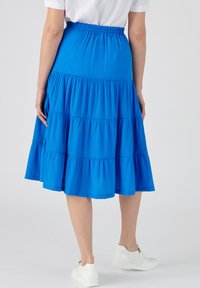 Falda azul de capas hecha de un tejido ligero con un acabado texturizado. Presenta una cinturilla elástica y cae por debajo de la rodilla.