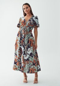 Robe maxi avec un décolleté en V profond, des manches bouffantes et une taille élastiquée. Elle présente un motif floral multicolore sur un fond sombre.