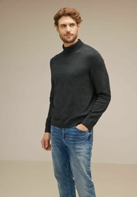 Mörkgrå polotröja i ett mjukt material, kombinerad med ljusblå jeans; enkel design och en åtsittande silhuett.