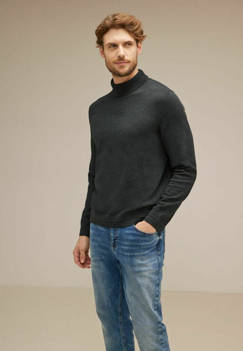 Mörkgrå polotröja i ett mjukt material, kombinerad med ljusblå jeans; enkel design och en åtsittande silhuett.