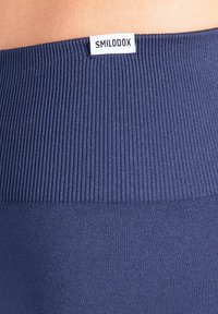 Marineblauwe leggings met een geribbelde tailleband, een gladde textuur en een merklabel. Het materiaal lijkt rekbaar en aansluitend.