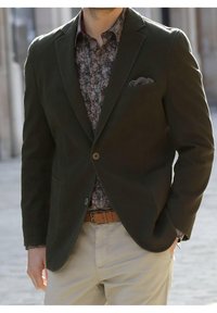 Dark green blazer with a textured finish, two front pockets, and a single button closure, worn over a patterned shirt and beige trousers.