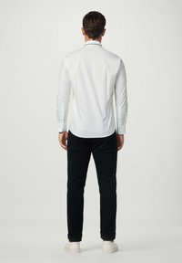 Witte lange mouwen shirt met zwarte accenten, gecombineerd met donkere broeken en witte sneakers. Het shirt heeft een slim fit en een gladde textuur.