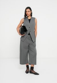 Γκρι προσαρμοσμένο γιλέκο με δύο κουμπιά, σε συνδυασμό με φαρδιά γκρι παντελόνια. Μαύρο clutch και υφασμένα μαύρα καλσόν αστραγάλου ολοκληρώνουν το σύνολο.