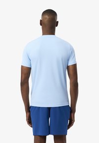 Maglietta atletica azzurro chiaro a maniche corte vista da dietro, realizzata in un tessuto liscio con scollatura a girocollo, abbinata a pantaloni corti blu navy.