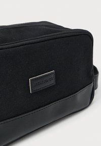 Μαύρο ορθογώνιο νεσεσέρ με κλείσιμο με φερμουάρ, κατασκευασμένο από ύφασμα και δέρμα, με ραμμένη ετικέτα "JACK & JONES" στο μπροστινό μέρος.