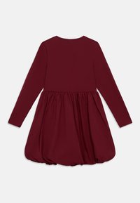 Μπορντό φόρεμα με μακριά μανίκια, εφαρμοστό τοπ και φουσκωτή, πτυχωτή φούστα. Μαλακή υφή με στρογγυλή λαιμόκοψη και ελαστικό στρίφωμα.