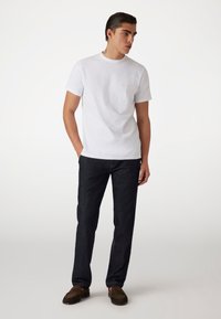Camiseta blanca de manga corta con cuello redondo y pequeño logo bordado, combinada con vaqueros de mezclilla azul oscuro y zapatos mocasín marrones.