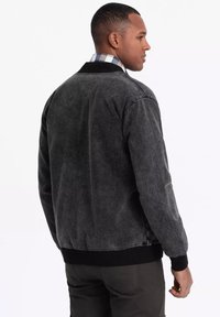 Musta corduroy-takki, jossa on ribattu kaulus ja hihansuut, joka tarjoaa sileän pinnan ja yksinkertaisen, klassisen muotoilun.