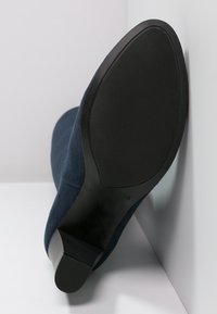 Dark blue ankle boot with soft suede upper, rounded toe, and a low, chunky black rubber heel. The textured sole provides grip.