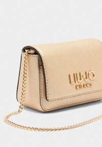 Sac banane en simili cuir doré avec une surface texturée, fermeture à rabat et une chaîne dorée en bandoulière ; présente le nom de la marque en relief à l'avant.