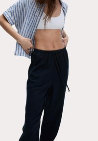 Bílý crop top s žebrovanou texturou, spojený s černými kalhotami na stahování. Pruhovaná modro-bílá košile s krátkým rukávem nošená rozepnutá.