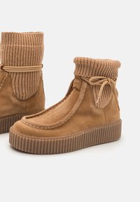 Bruna mocka ankstövlar med ribbad stickad krage, rund tå och tjocka texturerade sula. Har en båtdetalj och kontrasterande sömnad.