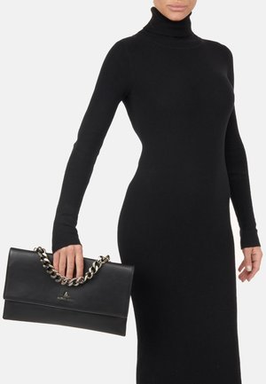 Borsa nera in pelle con tracolla in catena argentata, caratterizzata da una texture liscia e una chiusura a patta. La borsa è tenuta in una mano.