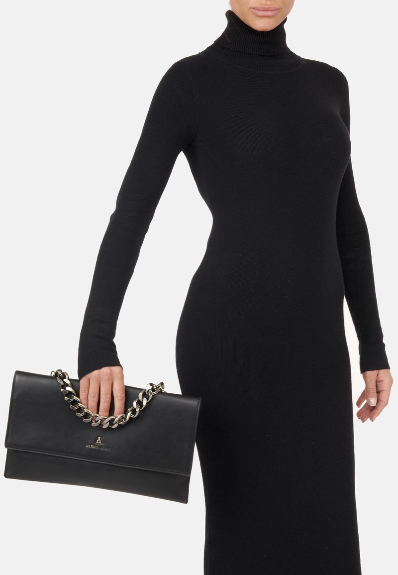 Czarna skórzana torebka na ramię z srebrnym łańcuchem, o gładkiej fakturze i zapięciu na klapkę. Torebka jest trzymana w dłoni.