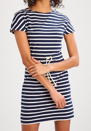 Frau trägt ein Kleid mit horizontalen dunkelblauen und weißen Streifen, kurzen Ärmeln und einem weißen Seilgürtel, der in der Taille gebunden ist.