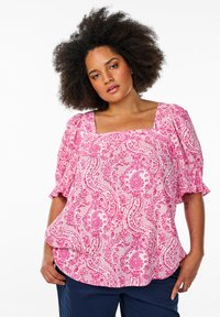 Bluzica s uzorkom u pink paisley boji, s kvadratnim izrezom i kratkim napuhanim rukavima. Izrađena od laganog materijala s lepršavim dizajnom.