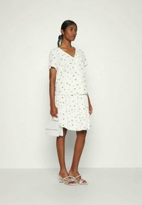 Vestido branco com mangas curtas, decote em V e padrão floral; saia em camadas; combinado com sandálias de tiras e uma pequena bolsa branca.