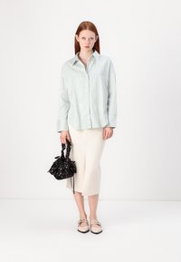 Lysegrønn rutet skjorte med knapper, kremfarget midiskjørt, blomstermønstret svart håndveske og beige flats med stropper. Enkelt design, myk tekstur.