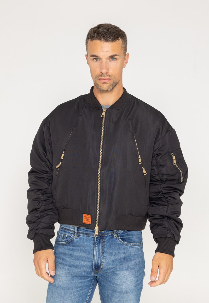 Czarna kurtka bomberka z zamykanymi kieszeniami, ściągaczami przy rękawach i u dołu, charakteryzująca się gładką teksturą oraz pomarańczową metką w talii.