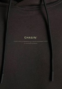 Sudadera gris oscura con cordones negros, que presenta el logo "CHASIN'" y un texto pequeño sobre desarrollo continuo e innovación tecnológica.
