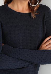 Marineblauer Strickpullover mit strukturiertem Muster, rundem Ausschnitt und langen Ärmeln. Bündchen und Saum sind gerippt für zusätzliche Details.