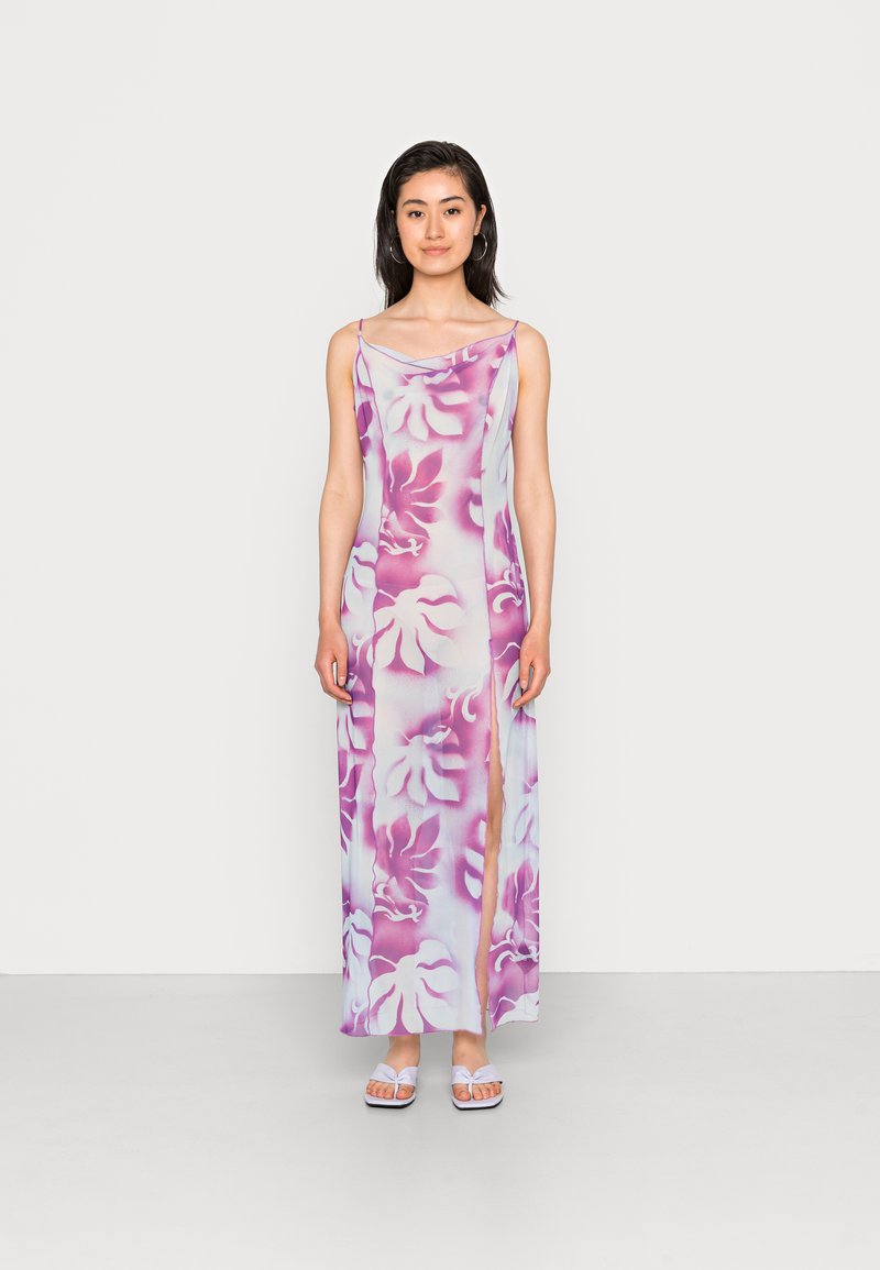 Vestido maxi de cetim com padrão floral em rosa e roxo, apresentando um decote drapeado e uma fenda lateral. Usado com sandálias brancas de slide.