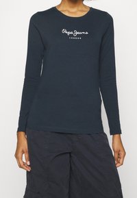 Dlouhý rukáv námořnické modré tričko vyrobené z bavlny, se středovým bílým logem "Pepe Jeans London" na hrudi. Kulatý výstřih a přiléhavý střih.