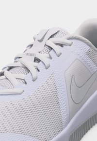 Λευκό αθλητικό παπούτσι Nike σε κοντινή λήψη που δείχνει το υφασμάτινο επάνω μέρος με υφή, τα κορδόνια και το γκρι λογότυπο Nike στο πλάι και στη γλώσσα του παπουτσιού.