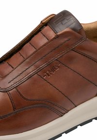 Baskets en cuir marron avec des détails cousus, des panneaux latéraux élastiques et une semelle en caoutchouc blanche. Présente un logo embossé sur le côté.