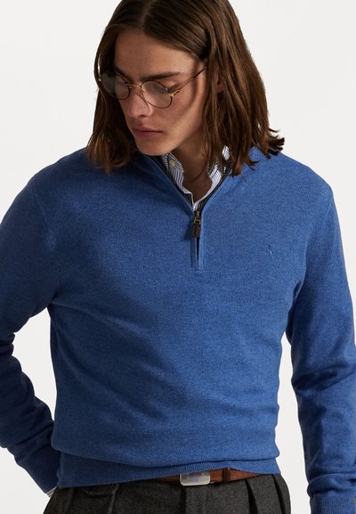 Blauwe pullover trui met een hoge kraag en een halve rits, gemaakt van een gestructureerd breimateriaal. Bevat een subtiel logo op de borst.