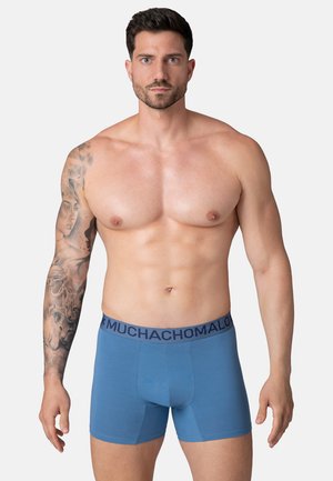 Modré boxerky s tmavým pásom, na ktorom je napísané "MUCHACHOMALO". Hladká tkanina, priliehavý strih a dĺžka po stred stehien.