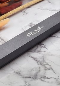 Scatola di gioielli nera con texture e finitura liscia, con il logo argentato "Sofia Milani Jewels", posizionata su uno sfondo bianco marmorizzato.