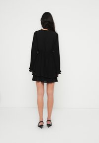 Μαύρο φόρεμα με μακριά μανίκια, εφαρμοστό μπούστο και στρώσεις με βολάν στο τελείωμα, με ζώνη στη μέση και ρέον, υφασμα με υφή.