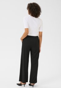 Schwarze weite Hosen mit strukturiertem Design, ausgestattet mit einem elastischen Taillenbund und Seitentaschen. Kombiniert mit einem schlichten weißen figurbetonten Oberteil.