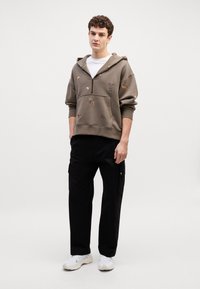 Sudadera con cremallera de color gris oscuro con motivos de animales bordados, combinada con pantalones cargo negros y zapatillas blancas. Textura suave y ajuste relajado.