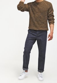 Brown textured sweater, navy tapered pants, and white sneakers. Sweater features a crew neck and ribbed cuffs; pants cuffed at the ankles.